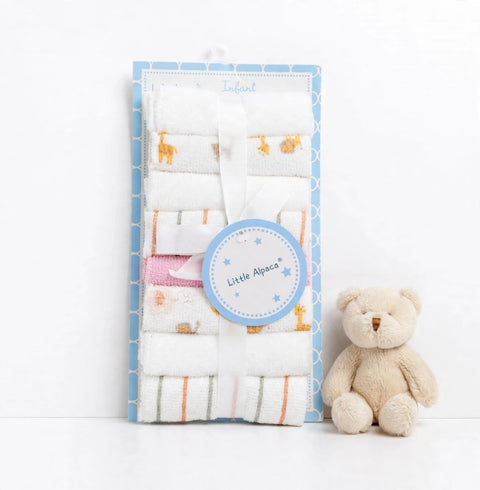 A packaged set of baby towels with small animal prints and striped patterns, tied with a white ribbon and a round 'Little Alpaca' tag, displayed next to a beige teddy bear on a white background.