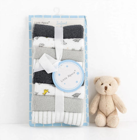 A packaged set of folded baby socks in dark gray, white, and light gray, tied with a white ribbon and a round tag, displayed next to a small beige teddy bear on a white background. The packaging is light blue with a geometric pattern and reads 'Little Apaca Infant'.