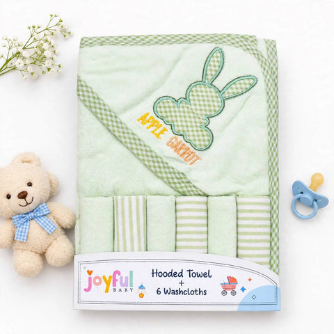 A folded light green hooded baby towel set with a bunny applique and the words 'APPLE CARROT' on the hood, shown with six matching washcloths. The set is packaged with a visible Joyful Baby label and styled on a white background with a teddy bear, baby flowers, and a pacifier.