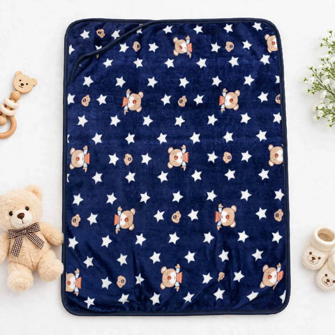 A navy blue fleece blanket with a white star pattern and teddy bear astronaut motifs, styled in a flat-lay with baby accessories on a white background.