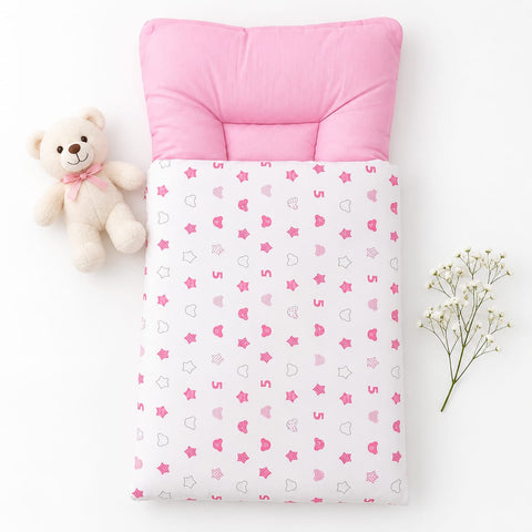 A baby sleep sack or quilt with a pink padded neck pillow, featuring a white base printed with pink hearts, stars, and crescent moons. The product is styled in a flat-lay arrangement with a small beige teddy bear on the left and baby's breath flowers on the right, set against a clean white background.