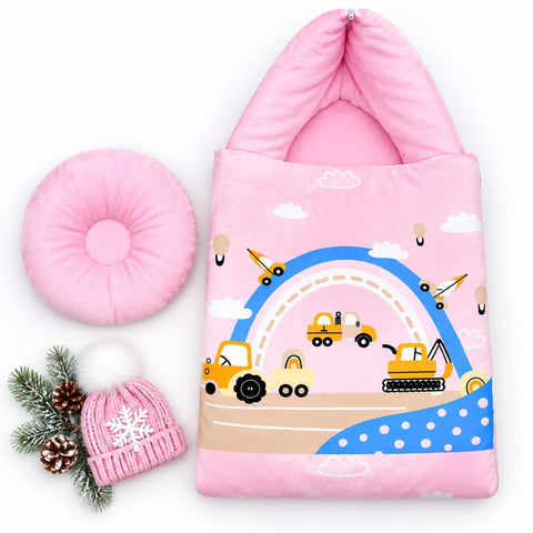 A pink children's sleeping bag or soft pouch with a construction-themed print, shown on a white background with a matching pink donut pillow and a pink knit hat with a snowflake, decorated with pine branches.