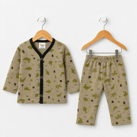 A two-piece baby clothing set including a long-sleeve button-front cardigan and matching pants, displayed on wooden hangers against a plain white background. The set features a beige base with an all-over green dinosaur and black star pattern, with a black trim on the cardigan.