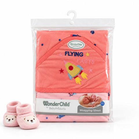 WonderChild 'Flying Fast!!' baby hooded wrap in coral pink with a rocket embroidery, shown in clear plastic packaging with a white hanger and pink booties with bear faces on a white background.