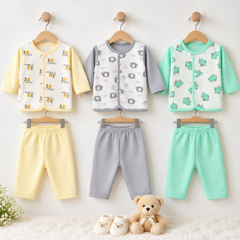 Three baby clothing sets hanging on wooden hangers against a white wall, each consisting of a short-sleeve vest and matching pants. The left set is pale yellow with a dog print, the middle set is light gray with a camera print, and the right set is mint green with a frog print.