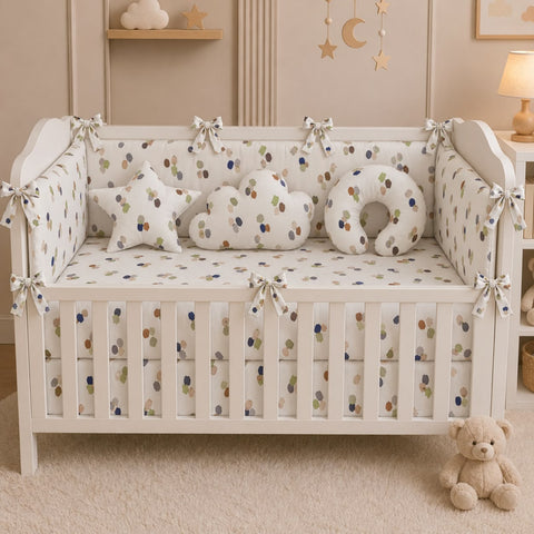 A white wooden crib with a matching crib bedding set featuring a small multicolor polka dot pattern, styled with star and cloud-shaped pillows in a warm, neutral nursery setting.