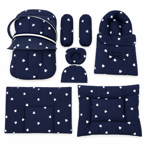 A 7-piece baby bedding set in navy blue with a white heart pattern, including a bassinet cover, mattress protector, footmuff, swaddle blanket, and various pillow and cushion protectors, arranged on a plain white background.