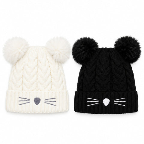 Two cable-knit pom-pom beanie hats on a white background, one cream with gray cat face details and one black with white cat face details.