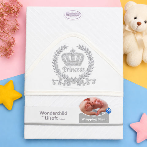Wonderchild by Lilsoft Princess wrapping sheet for newborn babies, featuring a white textured fabric with a silver embroidered crown and laurel wreath design. The sheet is displayed in a flat-lay setting with pastel pink, yellow, and blue background sections, decorated with a teddy bear, baby feet, and star cutouts.