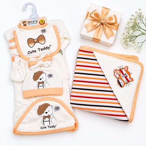 Baby gift set featuring a cream-colored footed sleeper with peach trim and a 'Cute Teddy' bear illustration, a matching bib, a small hat, and a striped baby blanket with peach trim, arranged on a white background with a gift box and baby flowers.