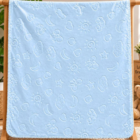 A light blue baby blanket with an embossed pattern of clouds, moons, stars, and suns, draped over a wooden hanger stand in a cozy room setting.