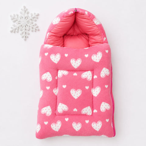 A pink quilted baby bootie or foot warmer with a white heart pattern, shown flat on a white background next to a white decorative snowflake ornament.