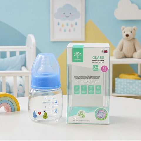A clear glass baby bottle with a translucent blue nipple top and printed measurement markings, shown next to its retail box on a white tabletop. The box reads 'Yashuay Glass Medall-neck Feeding Bottles' and says 80 mL.