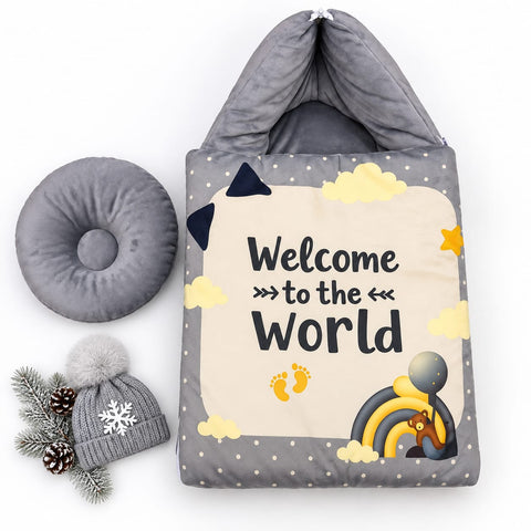 A baby welcome home sleeping bag set on a white background, featuring a gray hooded sleeping bag with a cream front panel that reads 'Welcome to the World' with yellow clouds, stars, footprints, and a rainbow. A matching gray donut pillow and a gray beanie with a pom-pom are displayed alongside.
