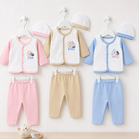 Three baby clothing sets hanging on white hangers against a light wall, each consisting of a sleeveless zip-front vest, pants, and hat. The left set is white and pink with a pink hat; the center set is cream and tan with a tan hat; the right set is white and blue with a blue hat.