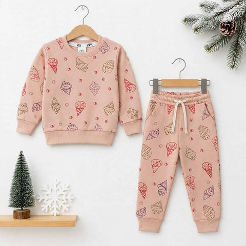 A children's two-piece clothing set consisting of a long-sleeve sweatshirt and matching jogger pants, both in a dusty pink color with an all-over ice cream cone print. The sweatshirt is shown on a wooden hanger, and the pants are shown on a metal hanger, arranged on a white background with decorative holiday props including a miniature Christmas tree, a snowflake ornament, and pine branches.