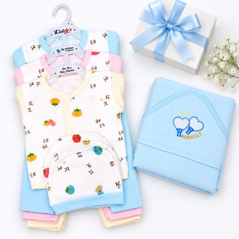 A baby clothing set arranged on a white background, including folded and hanging garments in pastel blue, pink, cream, and white with small fruit prints, plus a light blue hooded outfit with a heart design and the words 'TODAY IS A MIRACLE.' A white gift box tied with a blue ribbon and small white flowers are placed beside the set.