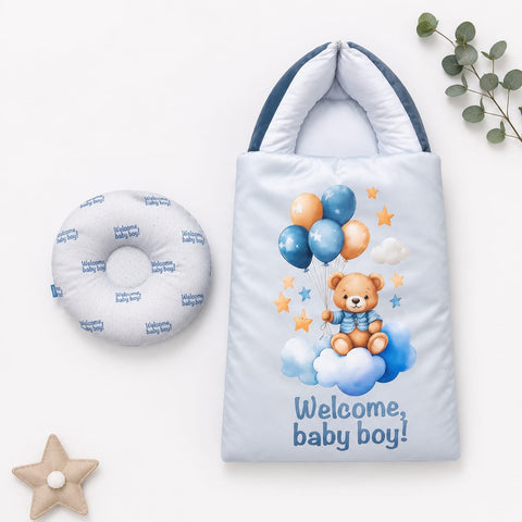 A baby welcome gift set featuring a light blue padded bag printed with a teddy bear, balloons, stars, and the text 'Welcome, baby boy!' alongside a matching circular cushion printed with 'Welcome baby boy!' repeated, styled on a white background with decorative eucalyptus and star props.