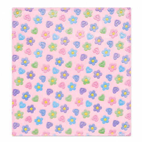 A square pink fabric item, likely a baby blanket or towel, featuring a repeating pattern of small 3D floral appliques in pastel shades of blue, purple, green, and pink with yellow centers.