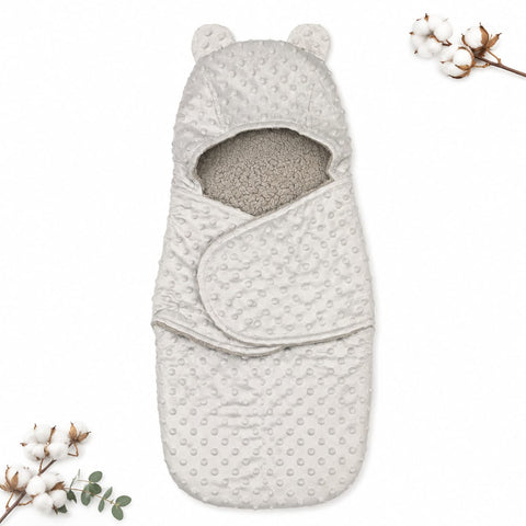 A baby footmuff in a light oatmeal gray color, featuring a textured minky dot pattern on the exterior and a soft, plush fleece lining visible at the opening. The footmuff is styled flat-lay with decorative cotton bolls on a clean white background.