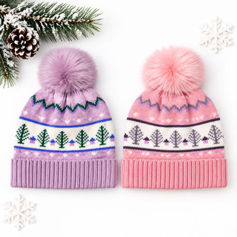 Two knit pom-pom beanies on a white background with seasonal props. The left beanie is lavender with green and blue Fair Isle tree patterns.