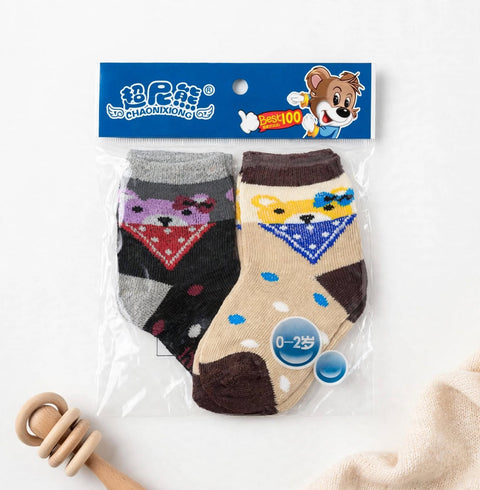 A pair of baby socks in clear plastic packaging with a blue header card. The socks are patterned with animal faces and colorful triangles, one in gray and black with a red/purple design, and one in beige and brown with a yellow/blue design.