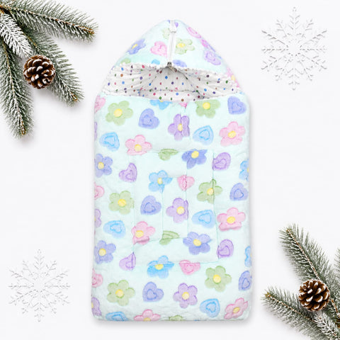 A hooded baby blanket or swaddle with a pastel floral print, styled in a flat-lay with pine branches, pinecones, and white snowflake decorations on a white background.