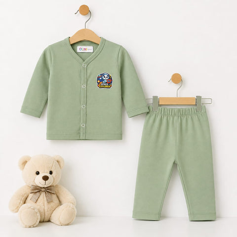 A baby clothing set consisting of a sage green long-sleeve cardigan and matching pants, displayed on wooden hangers next to a beige teddy bear. The cardigan features a colorful cartoon graphic on the left chest.