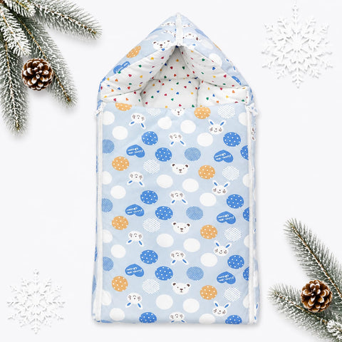 A baby hooded changing pad or burp cloth shown flat on a white background with decorative pine branches, pinecones, and white snowflakes. The fabric has a light blue base with white polka dots, blue polka dots, orange polka dots, and small cartoon animal faces including a rabbit, bear, and duck.