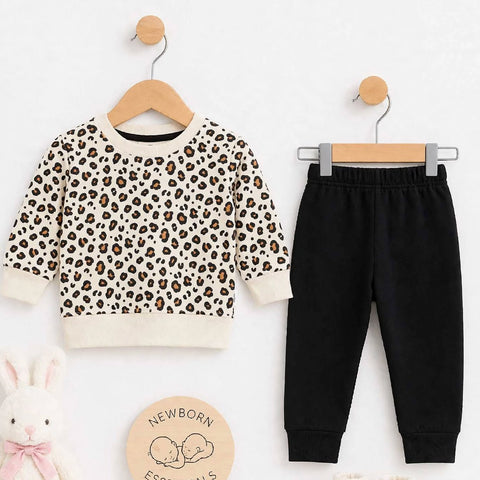 Baby clothing set featuring a long-sleeve leopard print sweatshirt, black jogger pants, and cream booties, styled on wooden hangers with a plush white bunny, a round wooden sign reading 'Newborn Essentials,' and a clean white background.