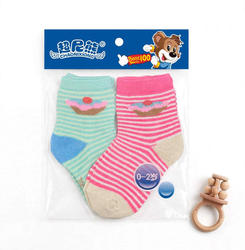 A pair of baby socks in a clear plastic package with a blue header card featuring a cartoon bear and Chinese branding. The socks are striped in mint green and pink, each with a small cupcake motif, and are shown alongside a wooden teether on a white background.
