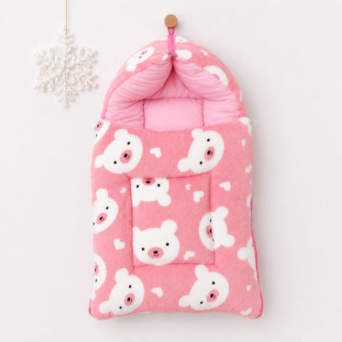 A pink plush baby foot warmer or bootie cover with a white teddy bear pattern, hanging from a wooden peg on a white wall next to a white snowflake ornament.