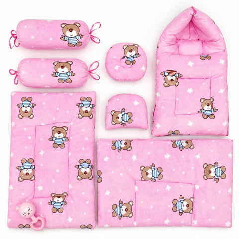 A coordinated baby bedding and accessory set in pink, featuring a teddy bear print. The set includes a baby blanket, a sleeping bag, a changing pad, two cylindrical pillow covers with tie loops, a round cushion, a small folded cushion, and a pink teething toy, all arranged on a plain white background.