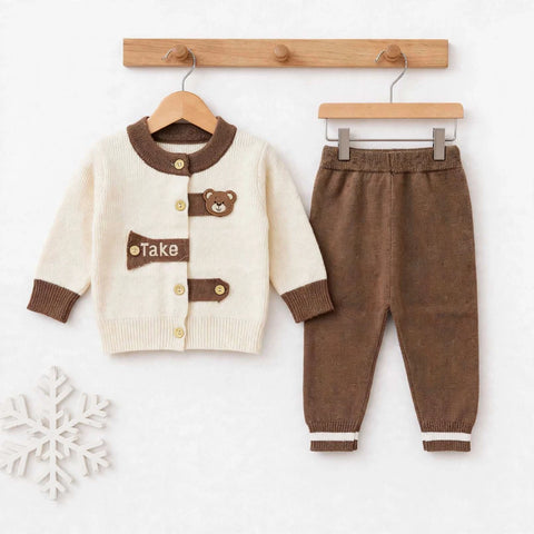 A baby clothing set consisting of a cream-colored cardigan with brown trim and a brown bear patch, paired with matching brown pants, displayed on wooden hangers against a white background.
