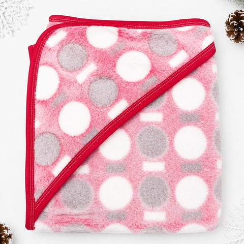 A folded plush hooded blanket in pink, white, and gray with a red border, photographed on a white background with small decorative holiday props in the corners.