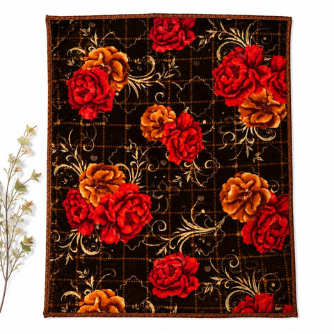 A rectangular textile or rug with a dark brown background, featuring large red and orange floral motifs and gold scrollwork, photographed flat against a white background with a small plant sprig at the left edge.