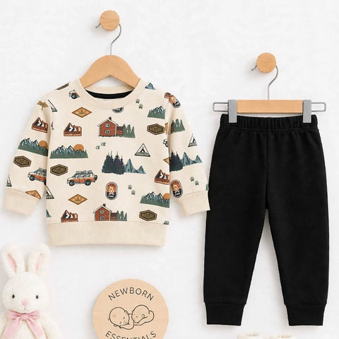 A baby clothing set displayed on a white background, featuring a cream long-sleeve sweatshirt with a rustic outdoor pattern, black jogger pants, cream booties, a plush white bunny toy, and a round wooden badge that reads 'Newborn Essentials'.