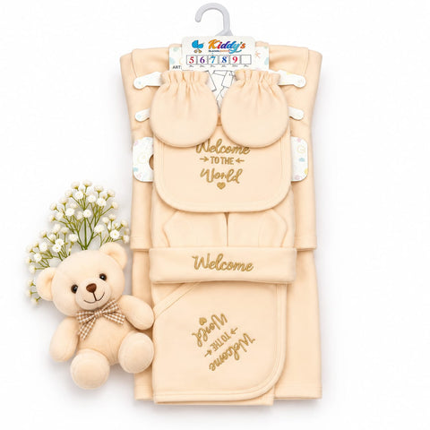 A baby welcome gift set including a beige blanket, matching booties, a footie, and a small plush teddy bear, displayed on a white background with a hanger tag.