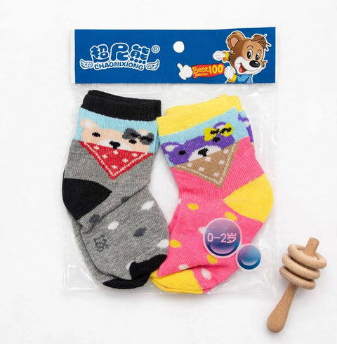 A pair of children's novelty socks in clear plastic packaging with a blue header card, shown alongside a small wooden honey dipper toy on a white background. The socks feature cartoon animal faces: one gray sock with a bear face and red bandana, and one pink sock with a purple bear face and yellow accents.