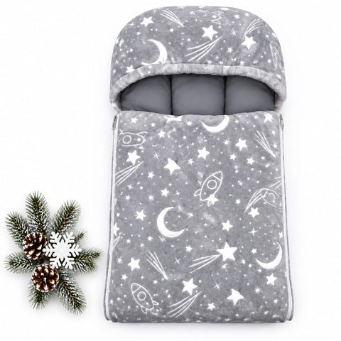 A gray plush baby sleeping bag or footmuff with a white space-themed print of stars, moons, and rockets, shown on a white background with a pine decoration in the corner.