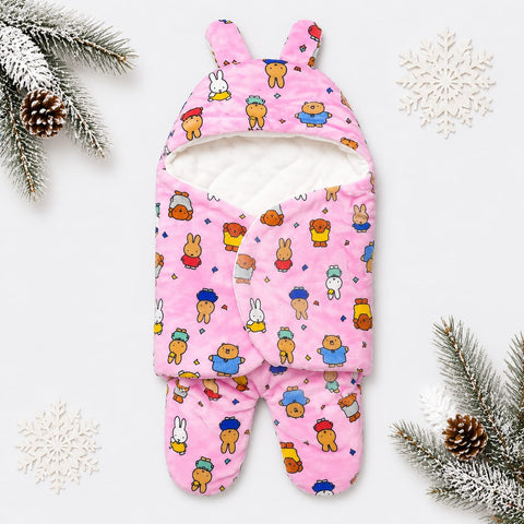 A pink footed baby sleep sack with bunny ears, featuring a playful cartoon bear and bunny pattern, styled on a white background with winter-themed pine branches and snowflakes.