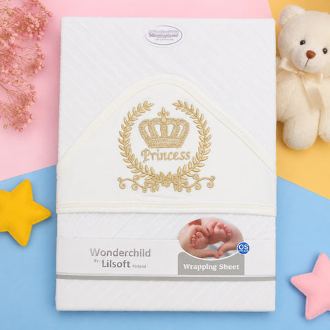 A white Wonderchild by Lilsoft baby wrapping sheet with a gold embroidered crown and the word 'Princess' on the front, styled in a flat lay with pastel pink, yellow, and blue sections, dried flowers, a teddy bear, and star-shaped props.