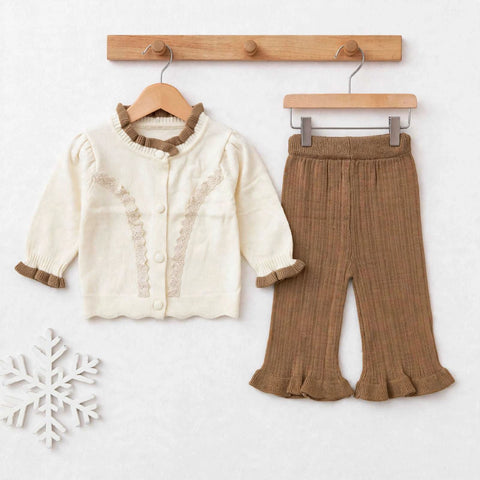 A toddler girl's two-piece knit outfit set featuring an off-white cardigan with brown ruffle trim and buttons, paired with brown textured flared pants with ruffle hems, displayed on wooden hangers against a light background.