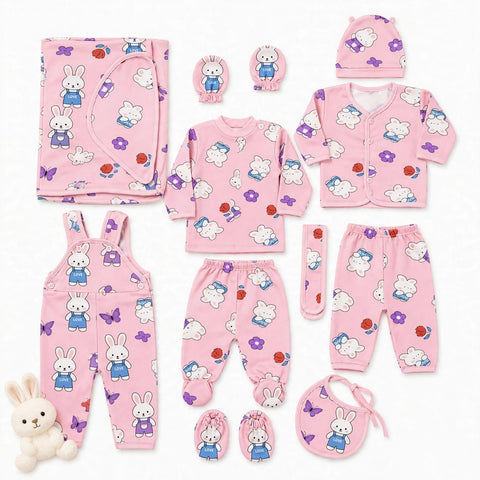 A coordinated baby clothing set laid out on a white background, including a pink long-sleeve top, matching pants, cardigan, hat, bib, booties, mittens, and overalls, all printed with white rabbits, purple butterflies, and small red/orange flower motifs. A small plush bunny toy sits at the lower left.
