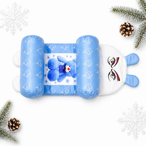 A blue and white bunny-shaped baby support pillow with a teddy bear graphic, styled on a white background with pine branches and snowflakes.
