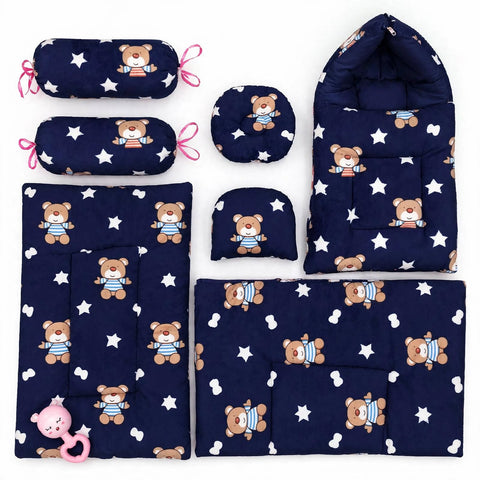 A 6-piece baby bedding set made of navy blue fabric with a white star pattern and a brown teddy bear print wearing a blue striped shirt. The set includes a bassinet cover, changing pad, footmuff, blanket, muslin cloth, and a pink teething ring.