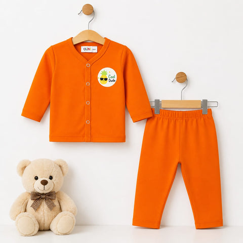 A baby clothing set consisting of a bright orange long-sleeve button-front cardigan and matching orange pants, displayed on wooden hangers against a white background, with a beige teddy bear sitting at the bottom left.