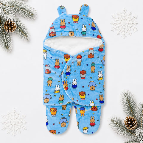 A blue baby hooded swaddle blanket with a playful cartoon bunny and bear pattern, styled flat-lay on a white background with pine branches, pinecones, and white snowflake decorations.
