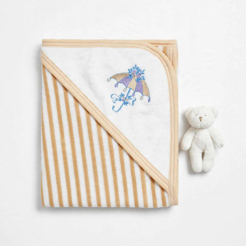 A folded baby hooded blanket with alternating cream and tan stripes, featuring a white hooded section with a purple and blue embroidered umbrella design. A small white plush teddy bear sits to the right on a clean white background.