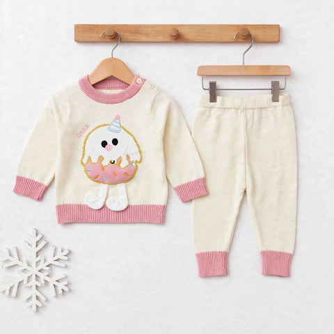 A baby knit two-piece outfit set consisting of a cream sweater with pink ribbed trim and a cute donut character applique, paired with matching cream pants with pink ribbed cuffs, displayed on wooden hangers against a light background.